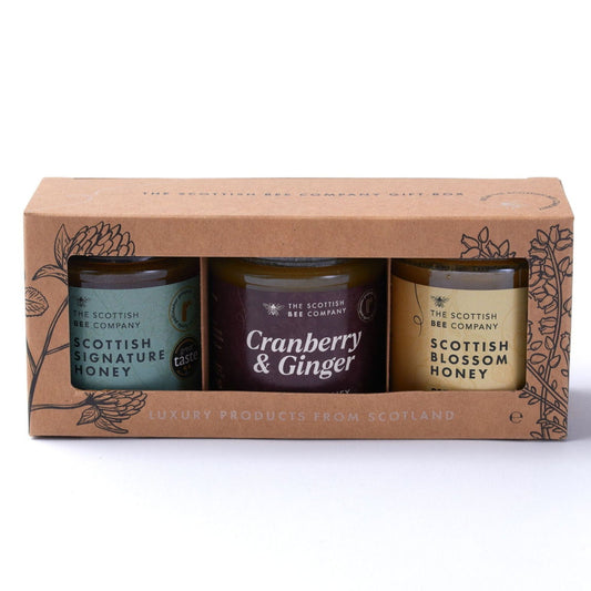 Three honey jars in a cardboard packaging with 'The Scottish Bee Company' branding on a white background. Includes Scottish Signature Honey, Cranberry & Ginger Blossom Honey and Scottish Blossom Honey