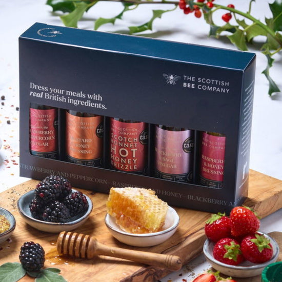 Honey product set from The Scottish Bee Company on a wooden board with honeycomb and berries.